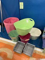 Photo showing seven storage bins including two Pottery Barn Kids canvas bins (pink and green), large green plastic basket, white round fabric bin with floral pattern, and two metal buckets.