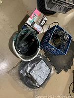 Overview of all items in the lot showing the bucket with tubing, blue crate with pump parts, Flotec hose packaging, and Flotec pump box.