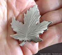 Front view of the sterling silver maple leaf brooch held in hand showing detailed vein engraving.