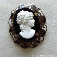 Front view of the oval black and white enamelled cameo brooch showing the female profile relief on black glass and scrolled enamel frame.