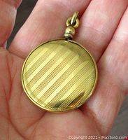 Front of the round gold locket showing engine-turned Art Deco diagonal stripes on the back surface.