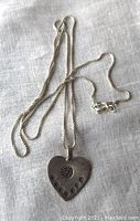 Front view of the heart pendant on the 18 inch chain displayed on a fabric background, showing detailed punched embellishments.