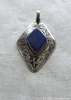 Front view of diamond-shaped sterling silver pendant featuring a rectangular lapis lazuli stone with gold flecks and engraved floral details.
