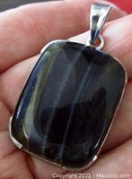 Front view of the sterling silver rainbow obsidian pendant held in hand showing the polished black stone with colorful flashes.