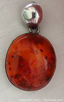 Front view of large oval cognac amber pendant showing rich amber color and inclusions with silver bail above.