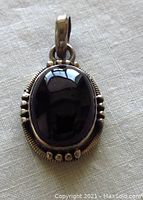 Front view of vintage sterling silver black onyx pendant showing polished oval black stone in ornate silver setting.
