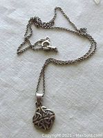 Sterling silver chain with Celtic pendant laid on white cloth background. Shows chain links and clasp.