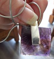 Photo showing the pendant held near a finger, highlighting the sterling silver bail and the purple amethyst quartz stone with inclusions.