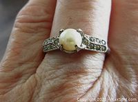 Front view of pearl ring on finger showing central round pearl and clear stones on band.