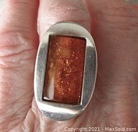 Close-up top view of the ring on finger showing rectangular amber cabochon and sterling silver setting.