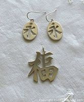Sterling silver good luck pendant and matching earrings set shown on white background, close up to show character design and marks.