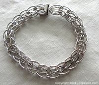 Full view of vintage sterling silver charm bracelet showing interlocking textured oval links and push-in clasp with safety latch.