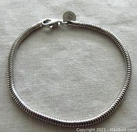 Sterling silver snake chain bracelet laid flat on fabric background, showing lobster claw clasp and marked plaque near clasp.