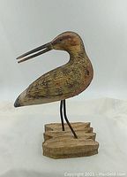Front and side views of carved wooden shore bird with natural paint tones, metal legs, and wooden base.