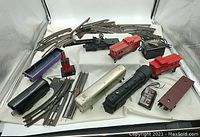 Photo showing multiple curved and straight track sections along with train cars, controllers, and parts spread on a white backdrop.