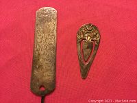 Both sterling silver bookmarks on red fabric background, showing size and decorative details