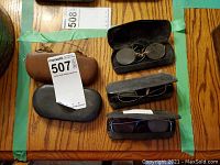 Top view of five antique glasses in cases on a wooden surface with MaxSold tags visible