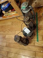 Photo showing all four kerosene lanterns on wooden floor next to shelving, each showing varying degrees of rust and wear.