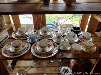 Top-down view of assorted fine china cups, saucers, and plates arranged on wooden shelves with floral and blue patterns predominantly seen.