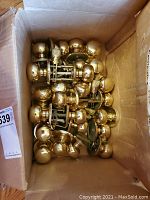 Top-down photo showing numerous brass doorknobs with attached mounting hardware inside a cardboard box.