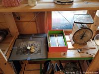 Photo showing vintage metal scale, framed group photograph with some pocket watches or similar items on top, box with glass projector slides, and metal clippers on wooden shelf.