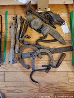 Overall lot showing multiple rusty iron horseshoes, wooden handled hooks, and pulleys arranged on a wooden floor