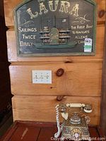 View of the full wooden wall plaque above the rotary phone showing steamboat model and text
