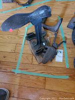 Photo showing an iron boot remover along with three cobbler's shoe stands set on wooden flooring.