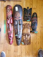 Full set of five carved wooden masks laid out on hardwood floor, showing different sizes and styles.
