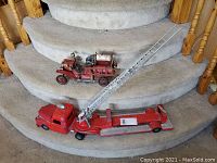 Both vintage fire trucks displayed together on carpeted stairs, showing relative size and condition.