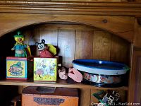 Shelf with vintage jack-in-the-box toys, plastic dolls, broken drum, and Mickey Mouse themed tray.