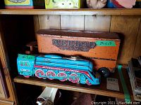 Photo shows vintage orange Allied Van Lines trailer toy truck and blue International Express toy engine on wooden shelf.