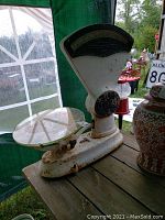 Side angle view of the vintage business scale showing white enamel body with rust and clear glass weighing platform on wooden surface.