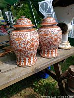 Pair of Chinese ceramic temple jars on a wooden surface outdoors, with visible lids and detailed pattern work in orange and white.