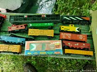 Overview of multiple HO scale model train cars on display including locomotives, caboose, gondola, autorack and boxcars in various colors with one still in original packaging.