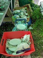 Red plastic bin containing white porcelain plates, a scalloped dish with a sailboat design, and small porcelain pieces including a creamer or sugar bowl.