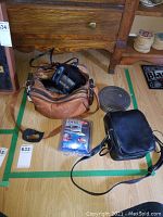 Image showing Kodak Colorburst 100 instant camera in brown carrying bag, Polaroid One camera in packaging, Kodak film canister, and black camera bag.