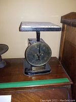 Front view of vintage Potter and Culver kitchen scale on wooden surface, showing large circular brass dial and rectangular metal weighing platform with tiles.