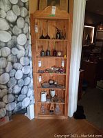 Wooden corner shelf unit filled with various vintage items, staged in a room showing its shape and size.