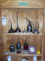Full view of two shelves holding assorted vintage metal oil cans and a small clock.