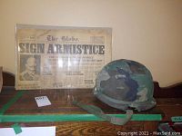 Full view of first newspaper in plastic sleeve alongside military helmet