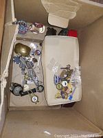 Photo of assorted small collectibles including pins, bottle openers, and keys arranged in a cardboard box