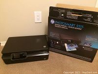 HP Photosmart 5515 printer beside its original box packaging showing branding and bundle edition