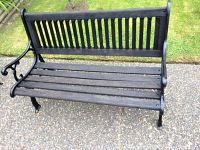 Full front view of antique garden bench showing black wrought iron frame with cedar slats for seat and backrest.