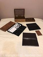 All four items shown on cream surface: two black wallets, a midcentury dark brown wallet, and an antique brown leather jewelry case with lid open and closed shown in different images.
