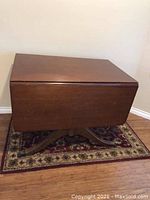 Dark polished wood dining table with two drop leaves on carved base on small decorative rug