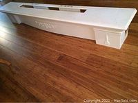 White wooden fireplace mantle shown from a front angle on wooden floor, displaying decorative molding and integration of fluorescent light top.