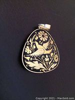 Close-up image of a triangular gold-tone pendant with hummingbird and floral engraving on black background.
