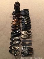 Photo showing an array of 17 pairs of women's footwear including boots, dress shoes, tap shoes, and casual sneakers displayed on carpeted floor.