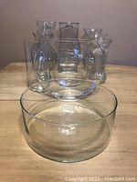 Front view of the 11 clear transparent glass vases arranged showing various shapes and sizes, placed on a wooden table.